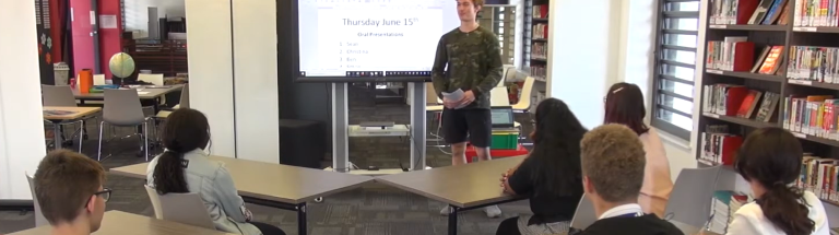 Student stands in front of presentation screen in front of class